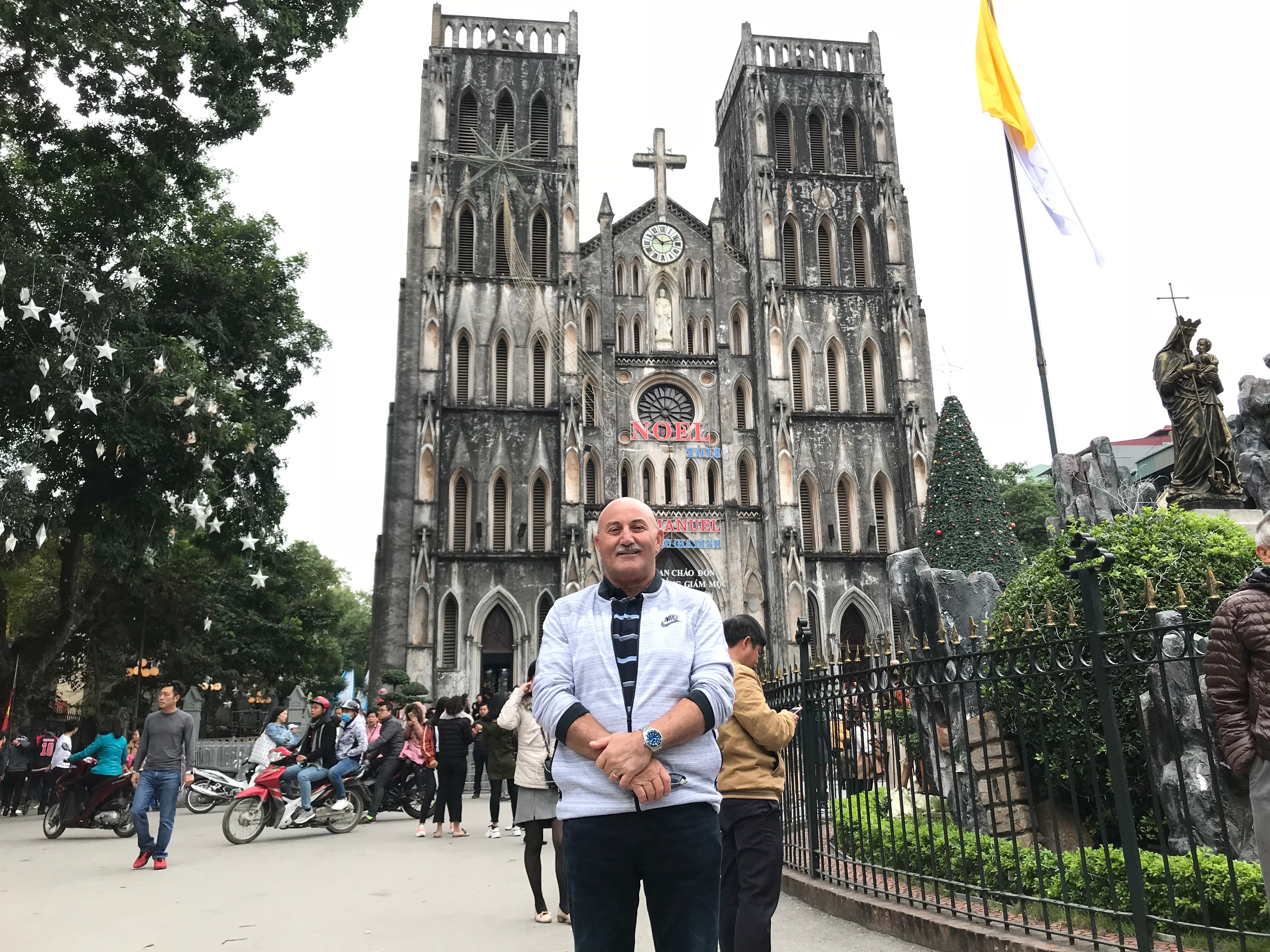 Australian man standing in front of a large cathedral Nha Tho in Hanoi after having dental smile makeover at top rated dental clinic in Hanoi, Vietnam with glamjet.com.au which is a global beauty, dental, and medical tourism booking platform .