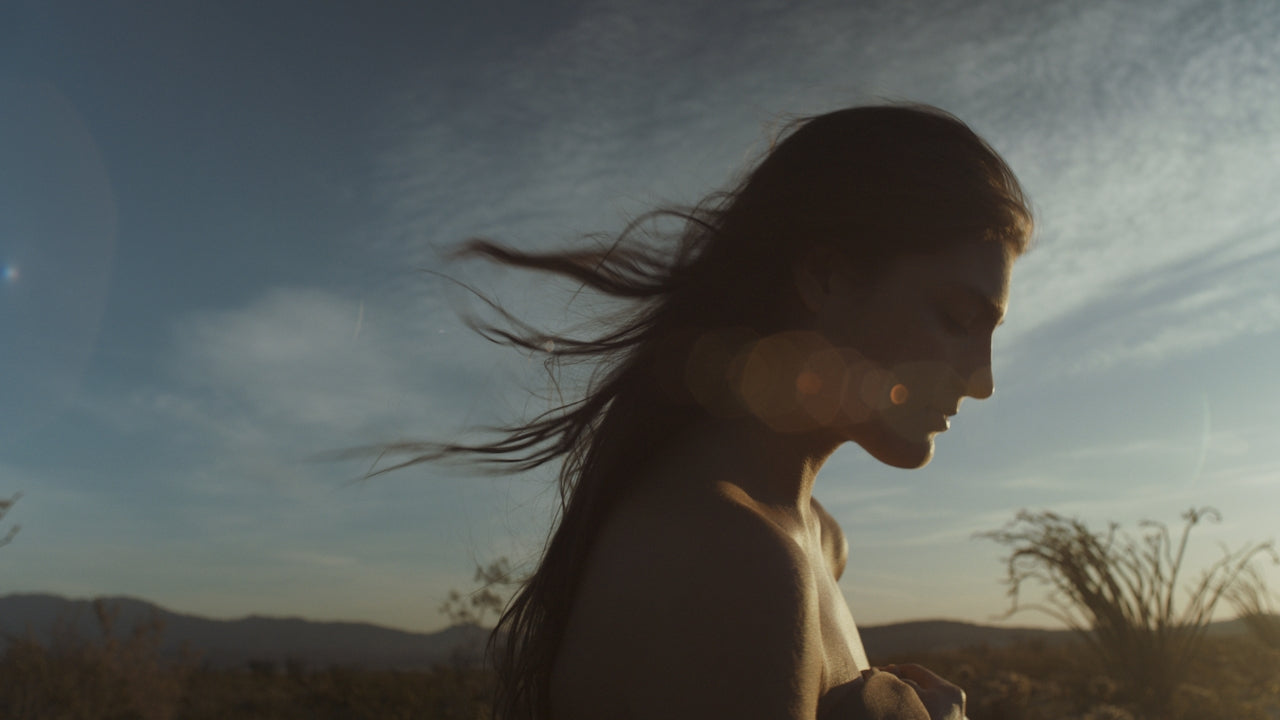 Woman with long hair standing in a desert landscape with mountains in the background. After transgender surgery for gender affirmations 